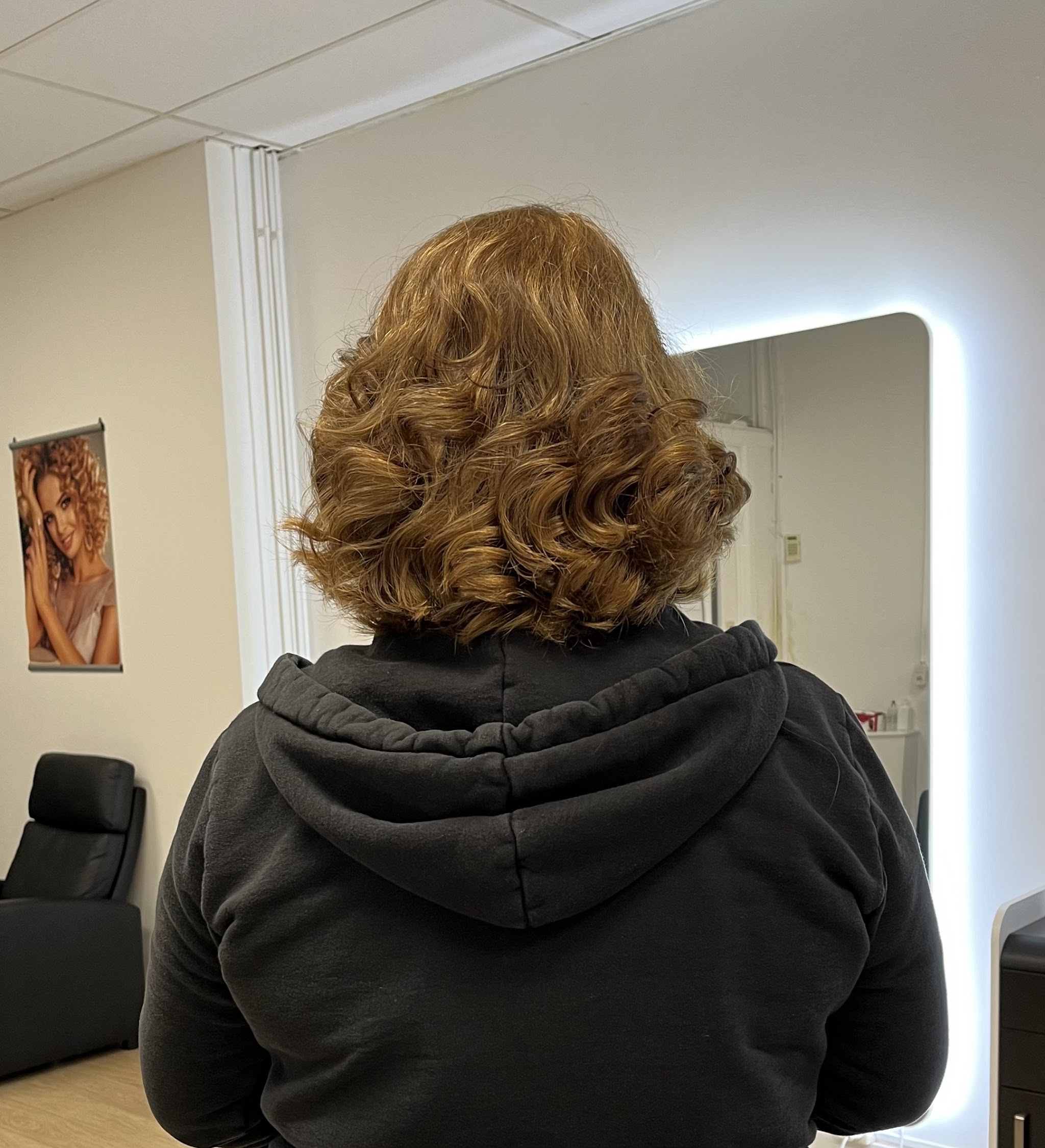 Korte koperbruine krullen van achteren gezien voor de verlichte spiegel